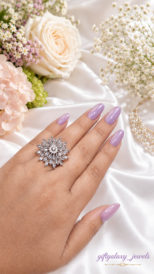 Hand wearing elegant silver crystal floral statement ring with pastel lavender nails and soft floral background.